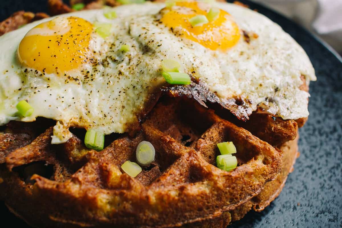 upclose shot of a crispy savory waffle topped with two fried eggs and green onions