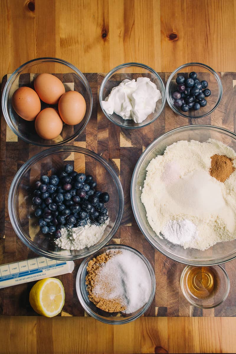 overhead shot of muffin ingredients with blueberries, lemon, eggs, sour c ream, almond flour cinnamon butter cinnamon and more