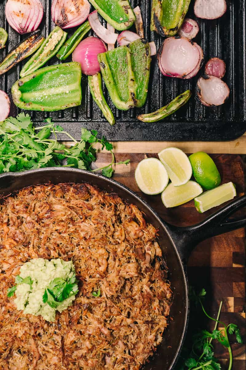 vegetables cilantro and limes with cooked pork carnitas in cast iron cookware
