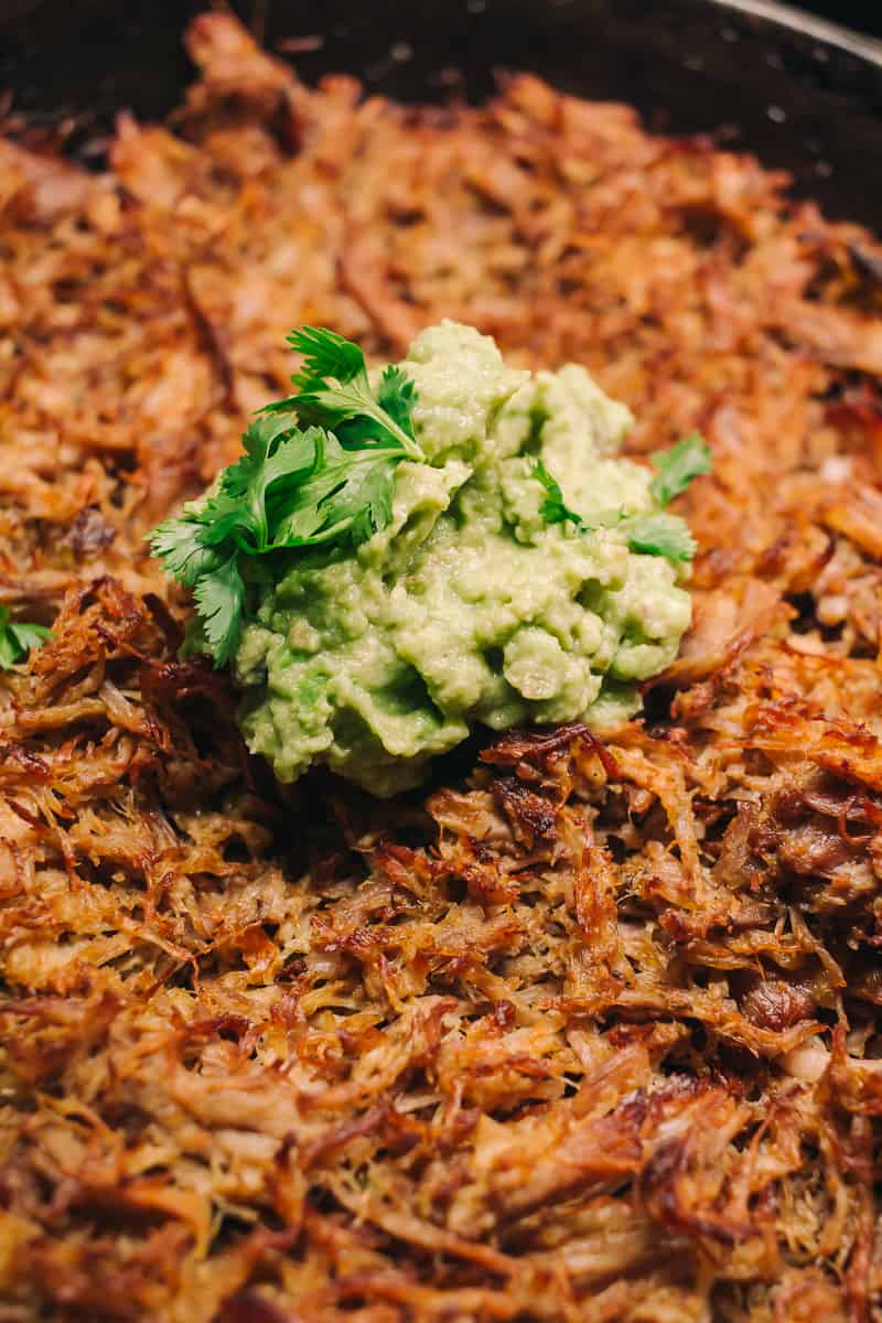 up close to crispy pork carnitas with a dollop of guacamole with cilantro