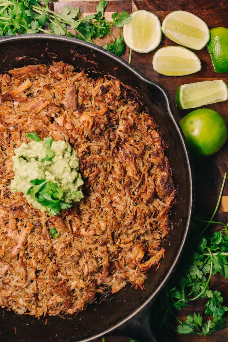 cast iron skillet with carnitas, guacamole and fresh limes