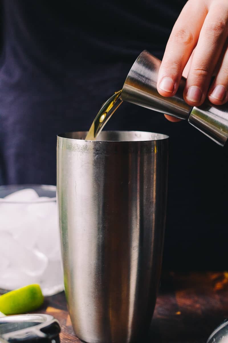 hand pouring jigger filled with rum into a cocktail shaker