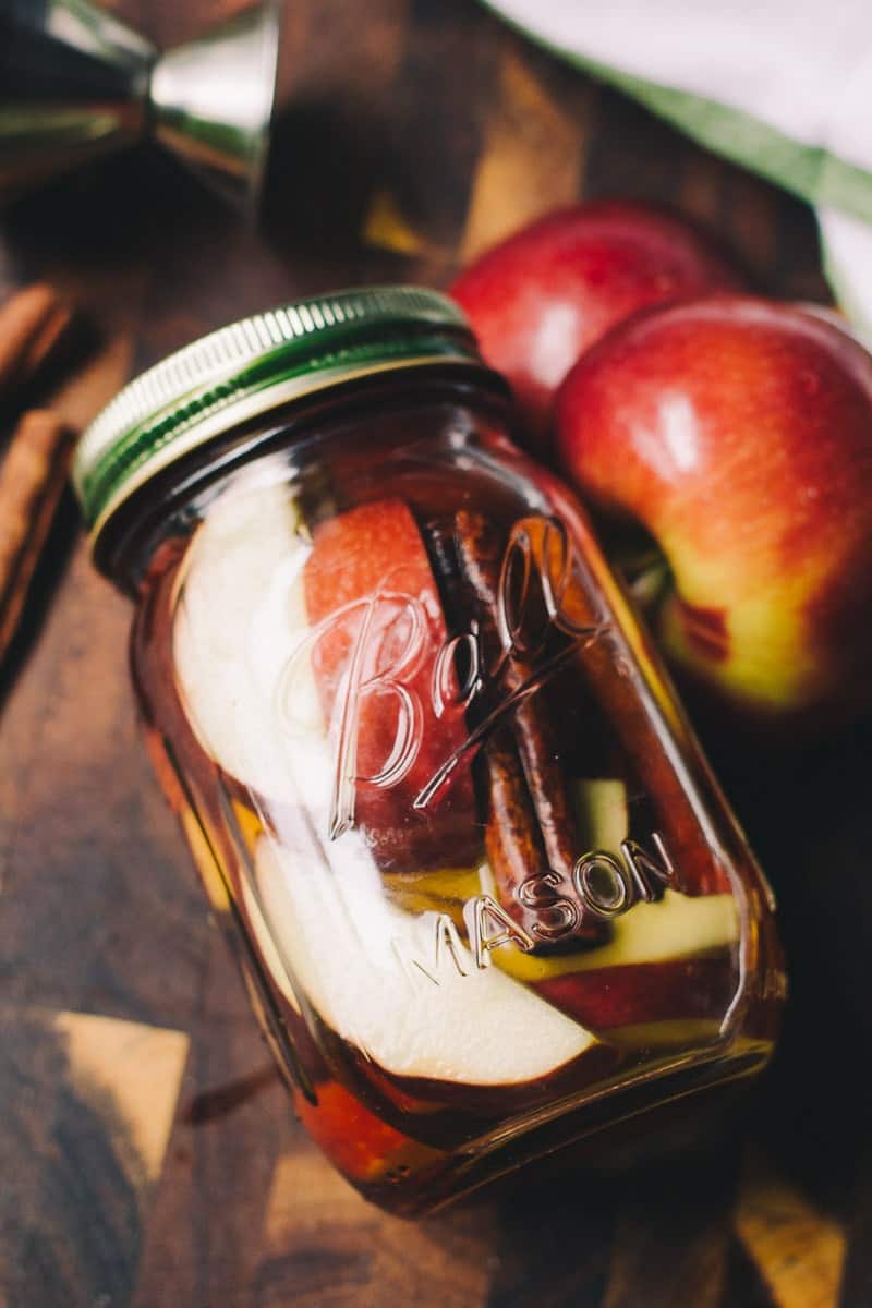 Apple cinnamon whiskey in a mason jar, surrounded by apples. 