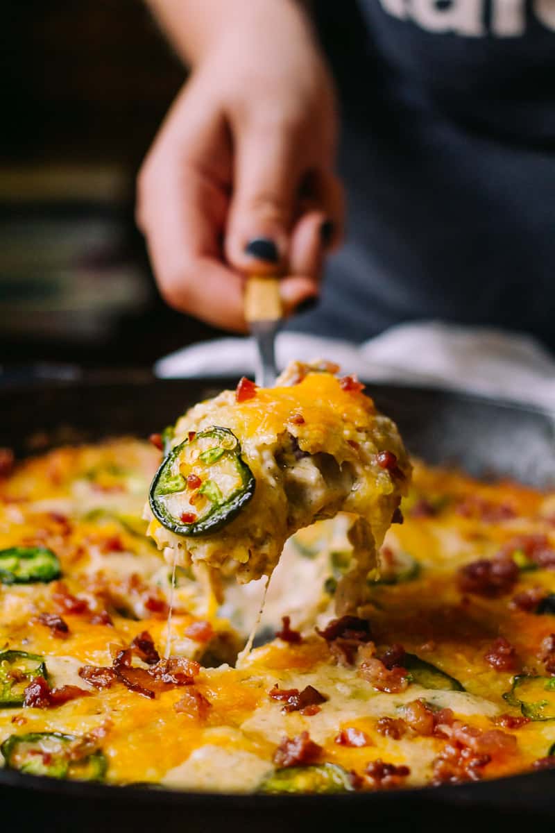Hand lifting cheesy jalapeno, bacon and chicken from a skillet