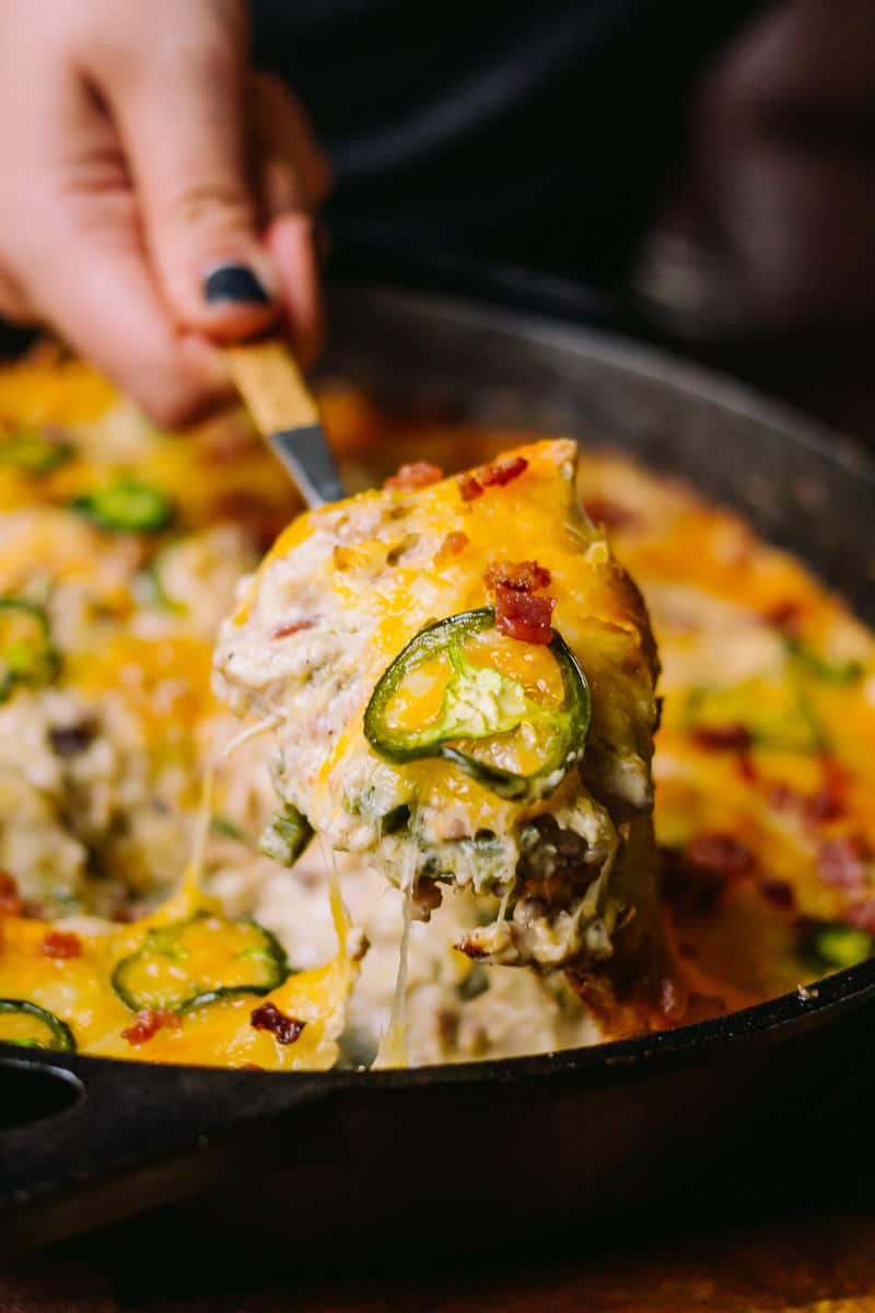 hand lifting chicken and cheese with jalapeños from a skillet