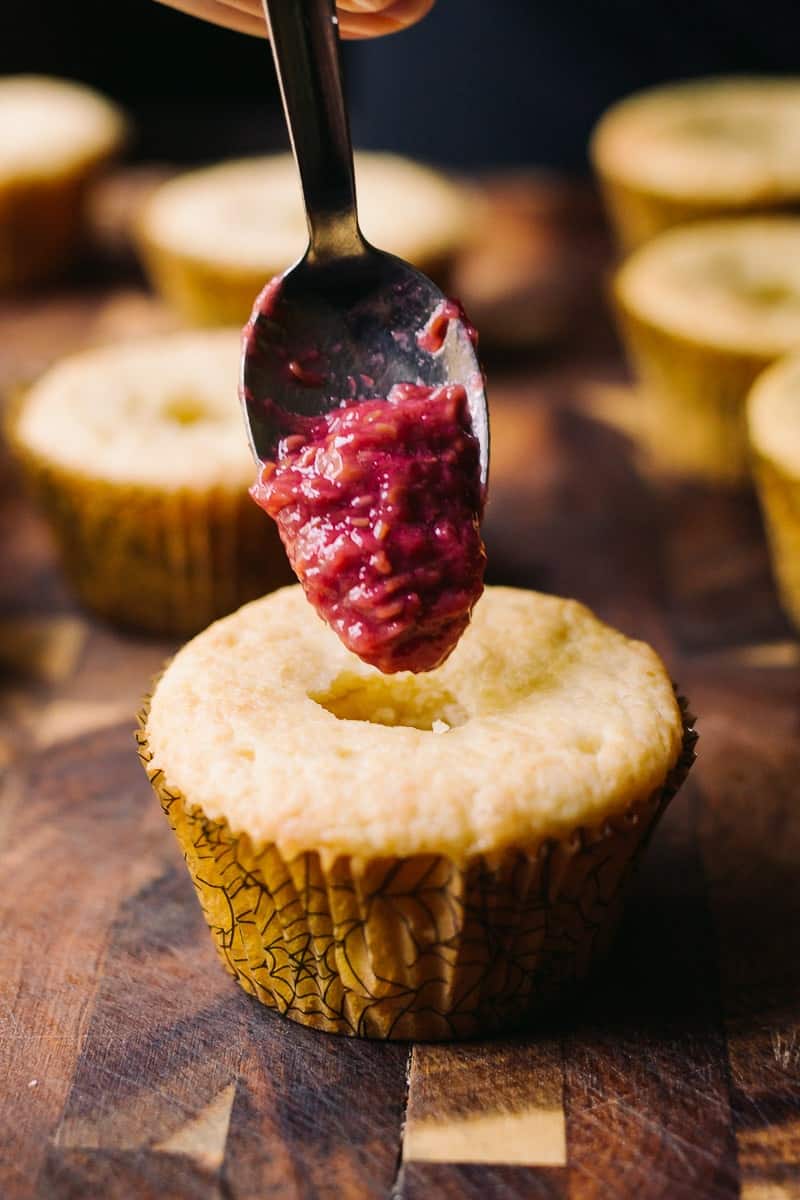 vanilla cupcake with raspberry jam on spoon, about to be filled