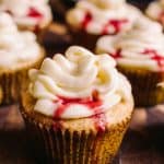Close up 45 degree photo of vanilla cupcake with cream cheese frosting and raspberry blood