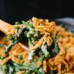 Wooden spoon holding green bean casserole with crispy onions