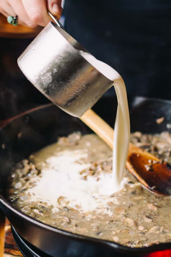adding heavy whipping cream to a skillet with mushrooms
