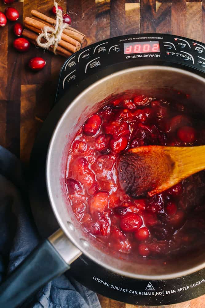 overhead of cranberry sauce boiling in a pot with a wooden spoon