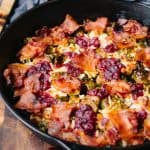 45 degree angle of cast iron skillet with bacon, cranberries and brussel sprouts