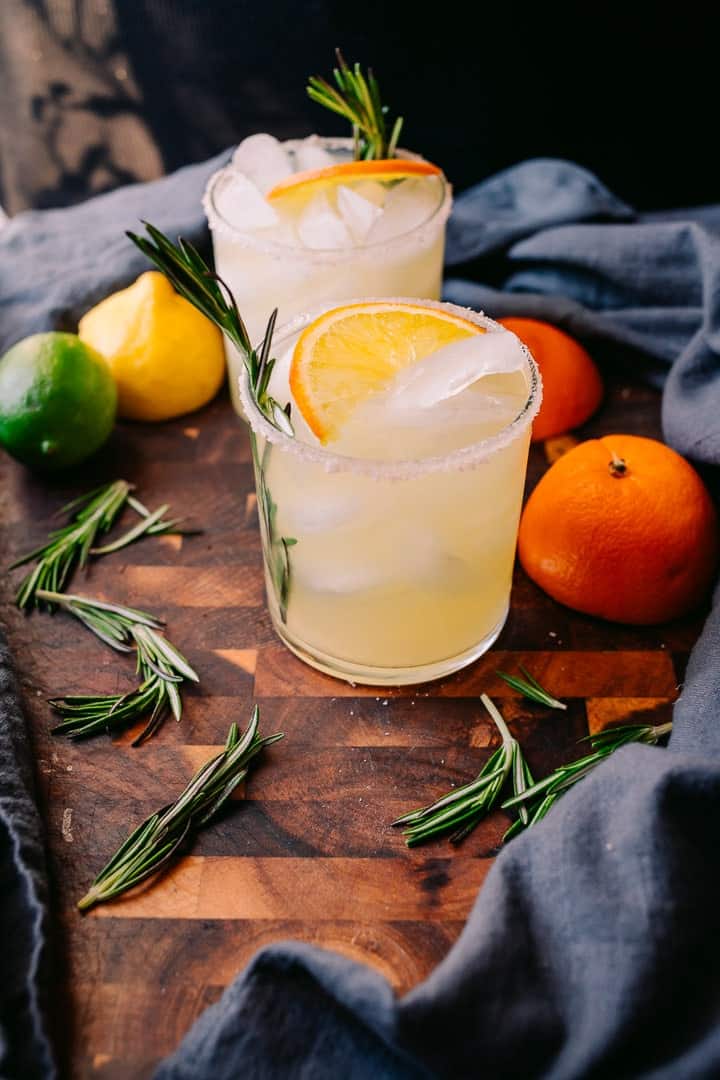 low carb rosemary margaritas on brown cutting board with fresh citrus and a grey napkin
