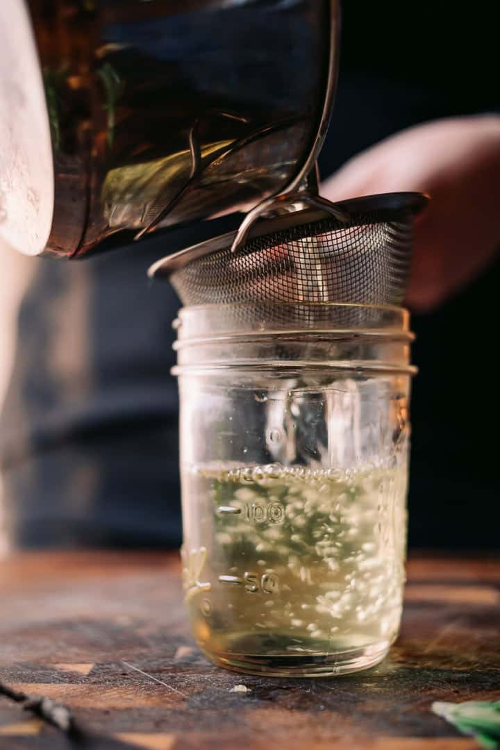 straining herbs from the syrup into a jar for rosemary simple syrup