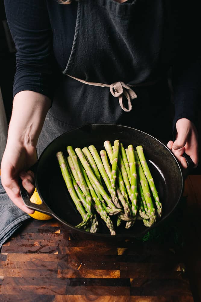 hands holding asparagus in a cast iron skillet