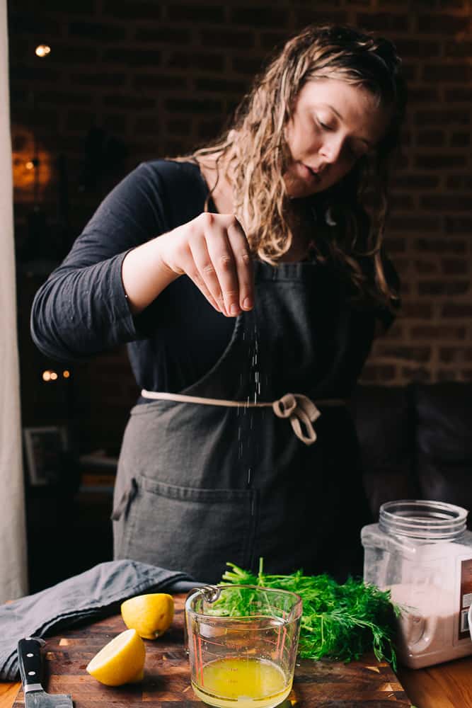 girl standing with an apron seasoning asparagus with salt