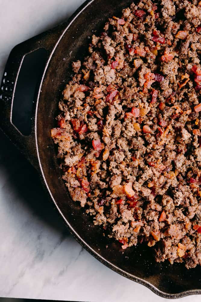 browned beef and bacon in a cast iron skillet