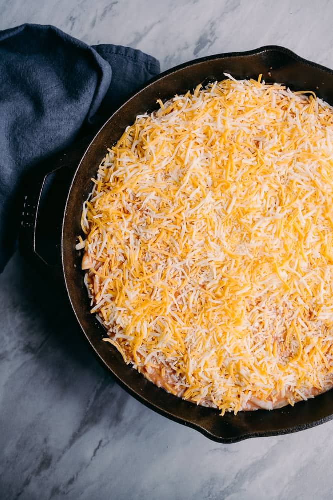 shredded cheese over top of a cheeseburger skillet in cast iron