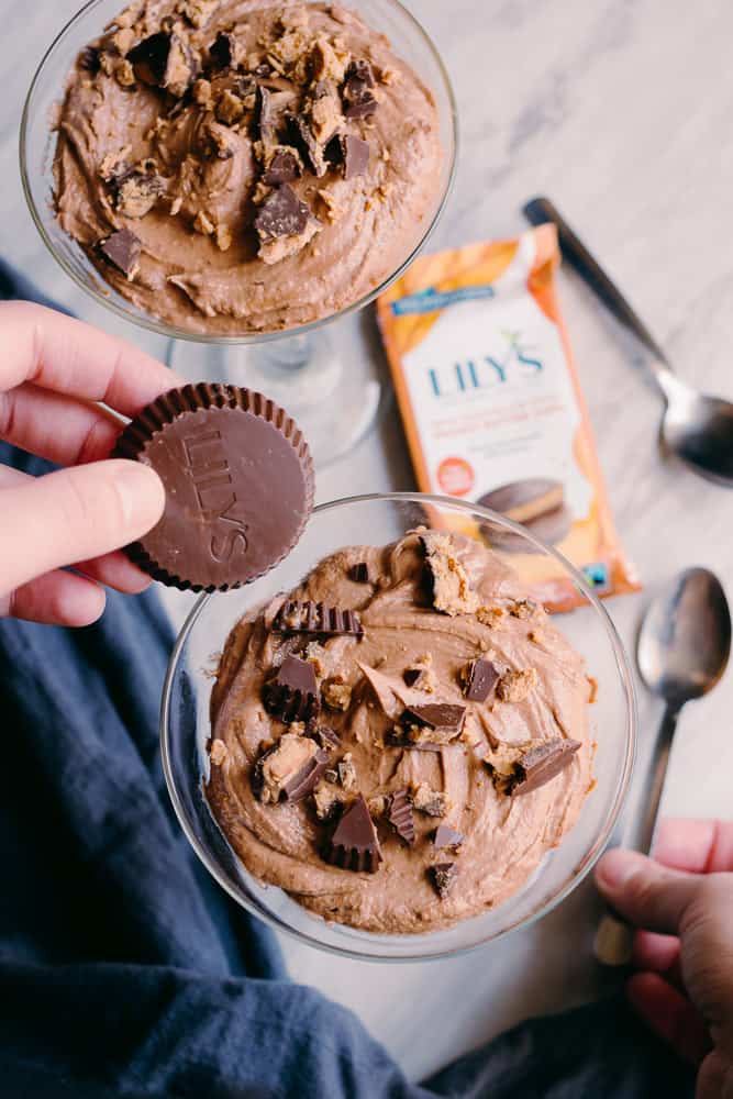 hand holding a lily's chocolate peanut butter cup over a glass of low carb chocolate peanut butter mousse