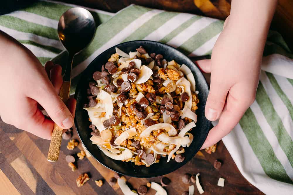 hands holding bowl of yogurt with toppings