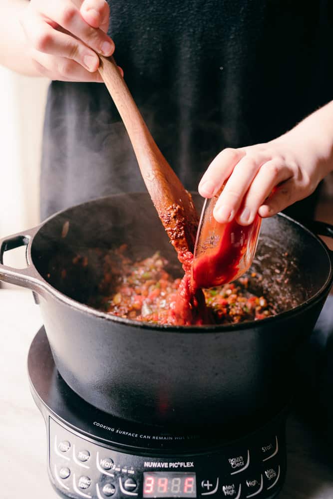 adding tomato paste to a dutch oven with peppers