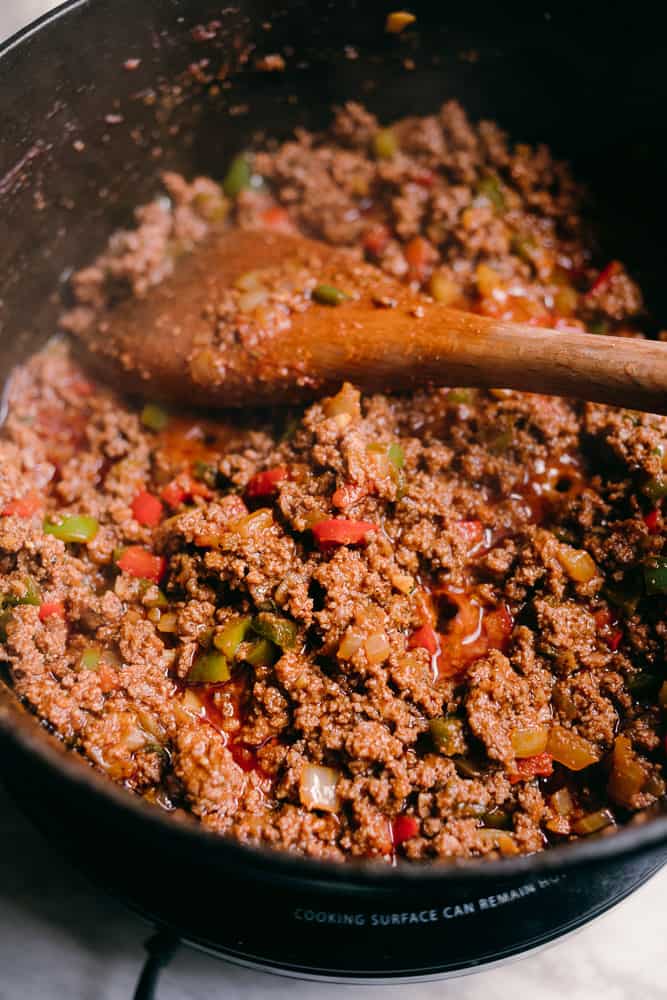 cooked ground beef with red bell peppers and a wooden spoon