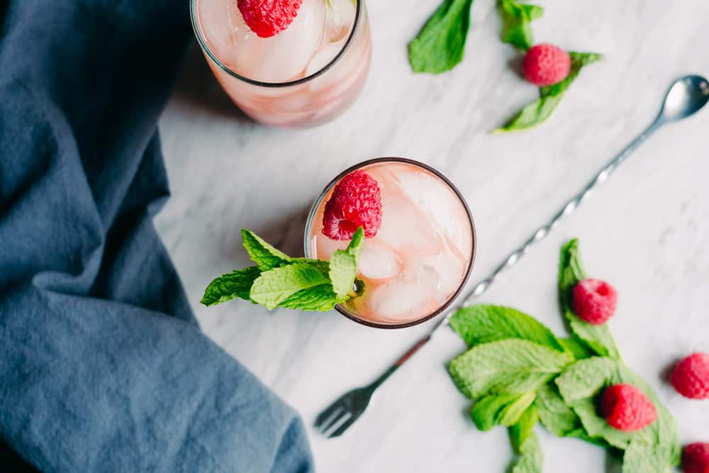 two raspberry cocktails with mint leaves a grey napkin and a bar spoon