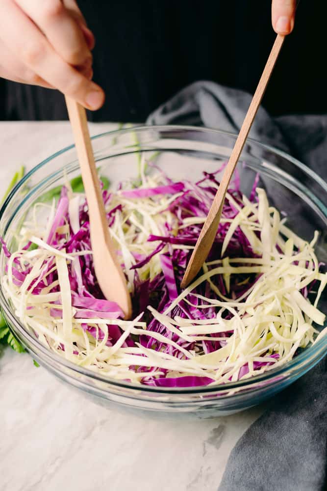 mixing purple and green cabbage with wooden spoons
