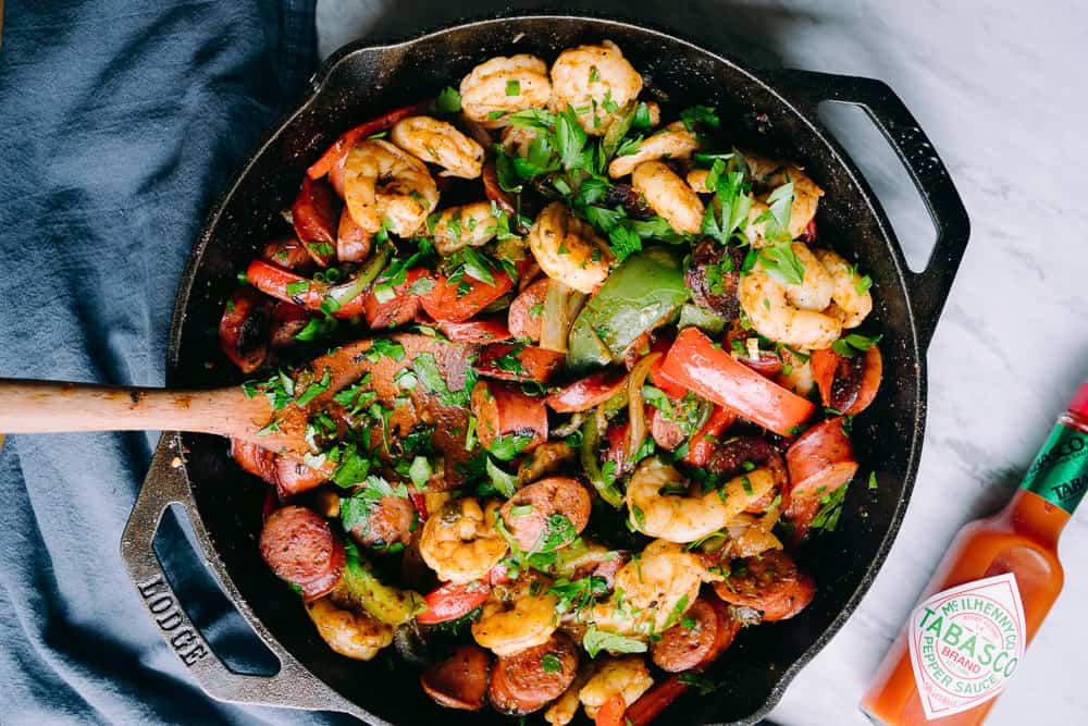 flatlay of cast iron skillet with tabasco sauce, shrimp peppers and sausage