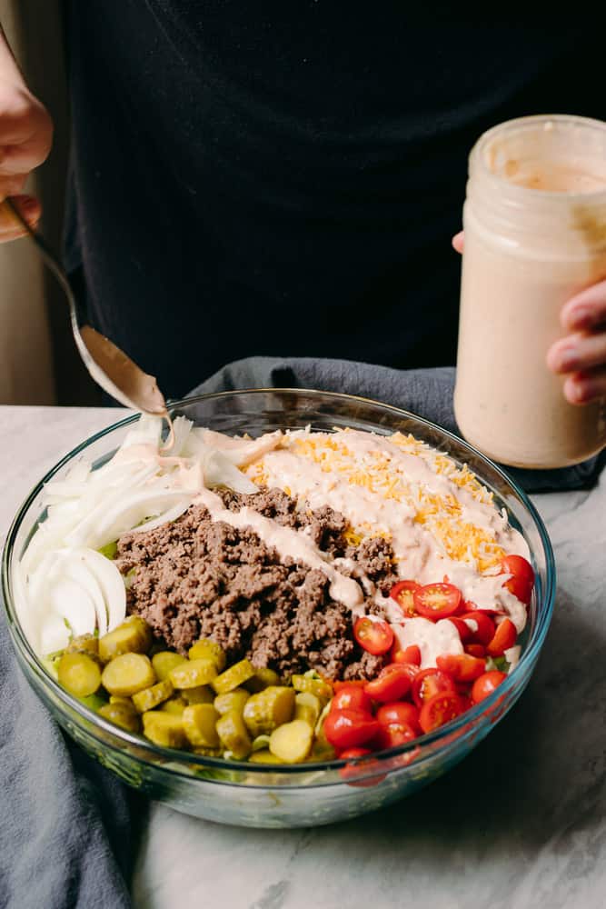 spooning on thousand island dressing onto a cheeseburger salad