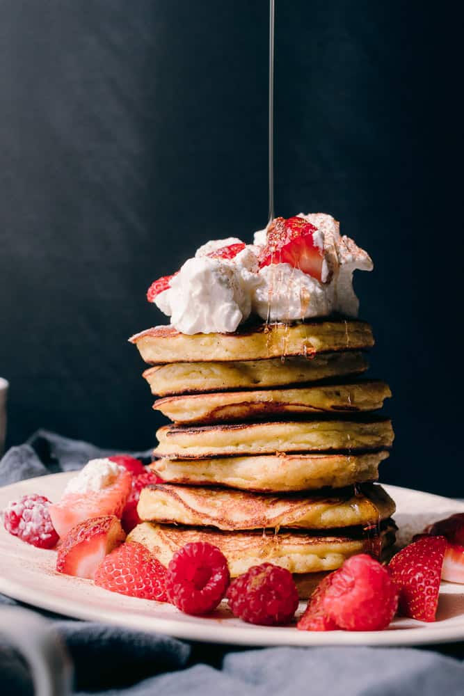 stack of pancakes with berries whipped cream and maple syrup drizzle