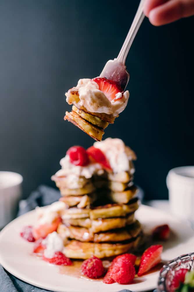 forkful of pancakes with strawberries and whipped cream