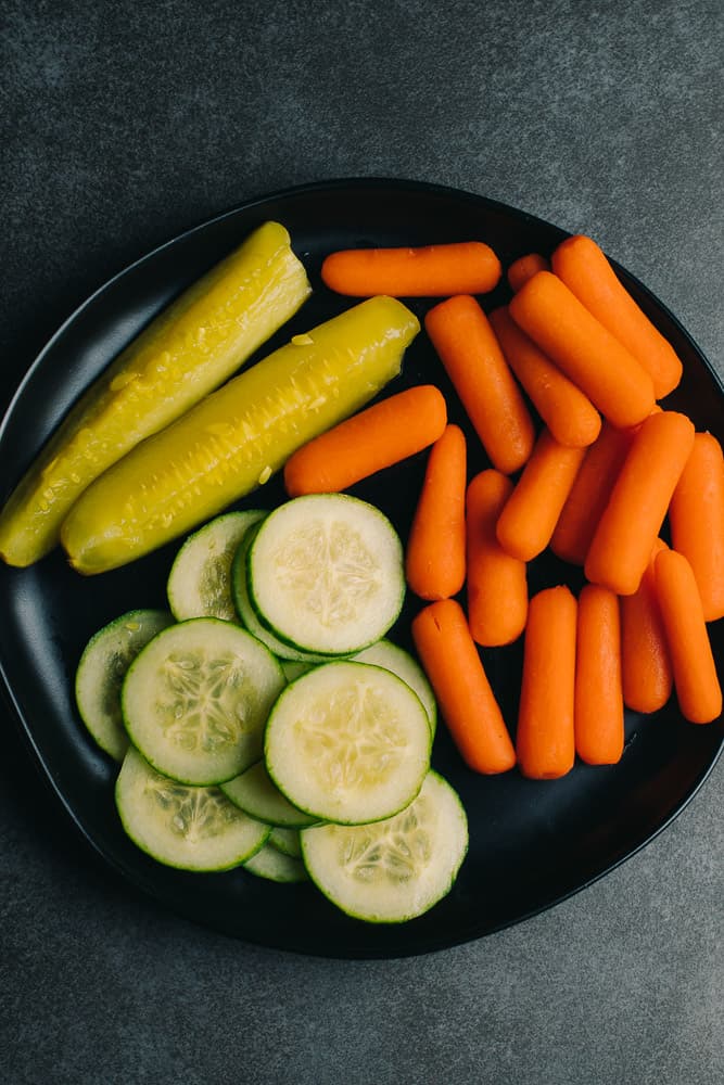 carrots pickles and cucumbers on a black plate