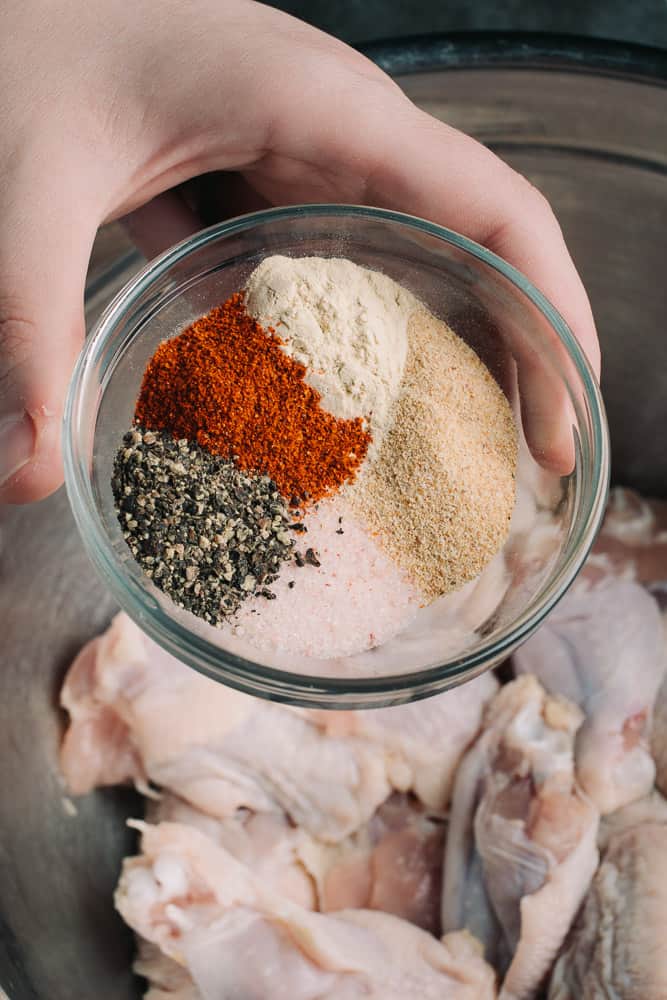 hand holding seasoning blend with raw chicken wings in back