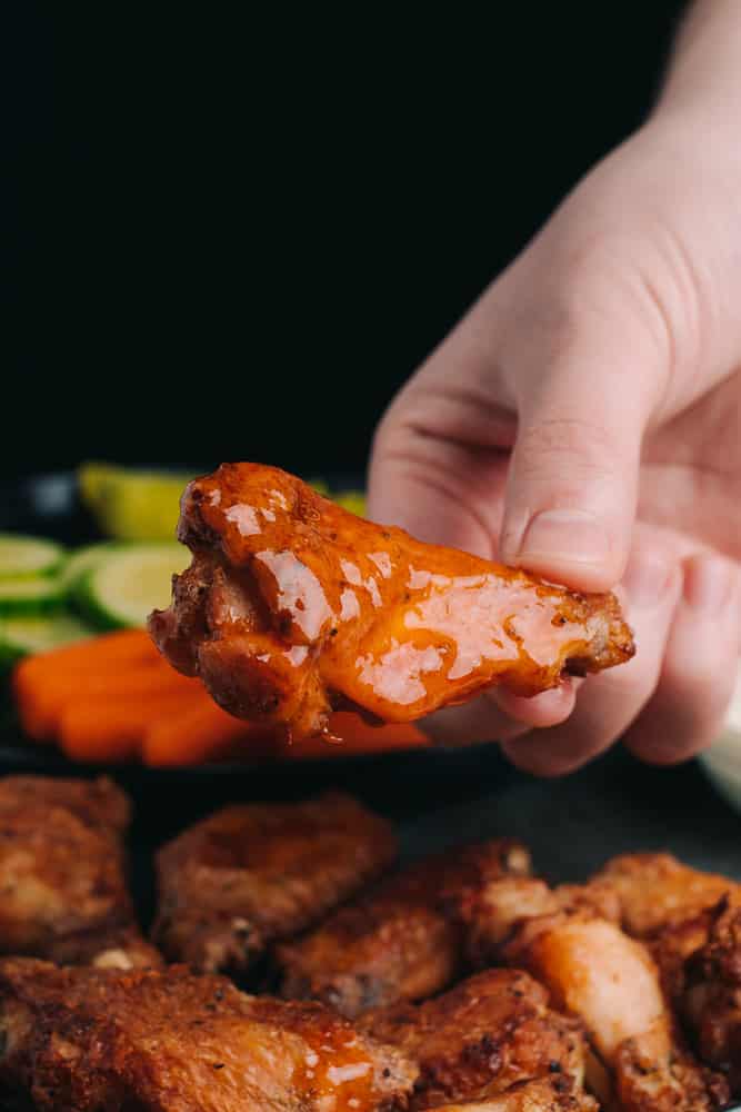 hand holding a baked chicken wing with buffalo sauce