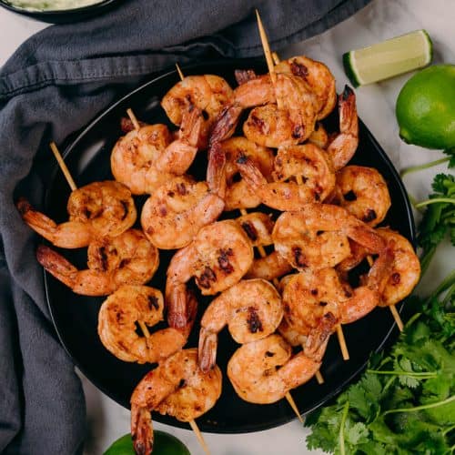 chipotle lime shrimp skewers with grey napkin limes and cilantro