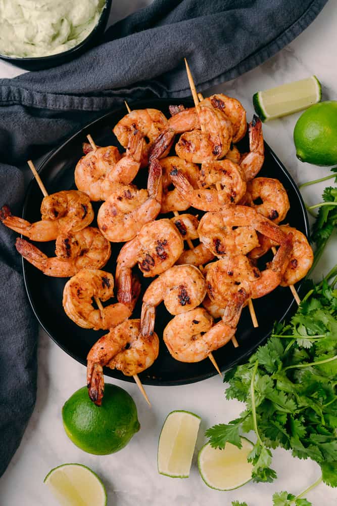 chipotle lime shrimp skewers on a black plate with limes