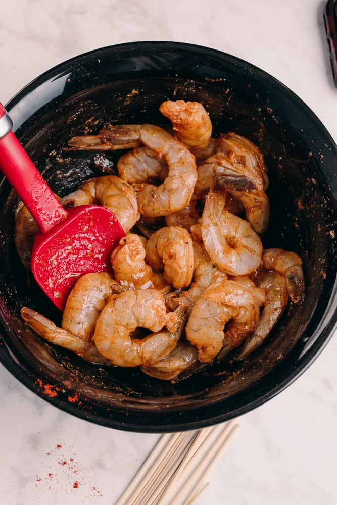red rubber spatula combining seasoned shrimp in a black bowl