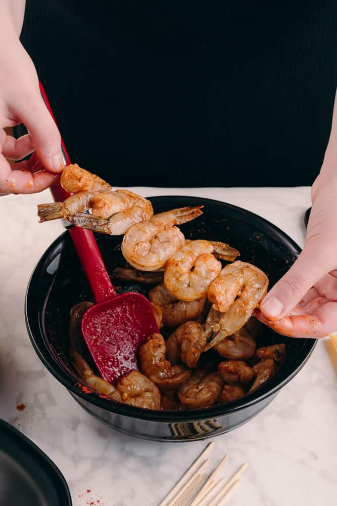 adding shrimp to skewers to grill