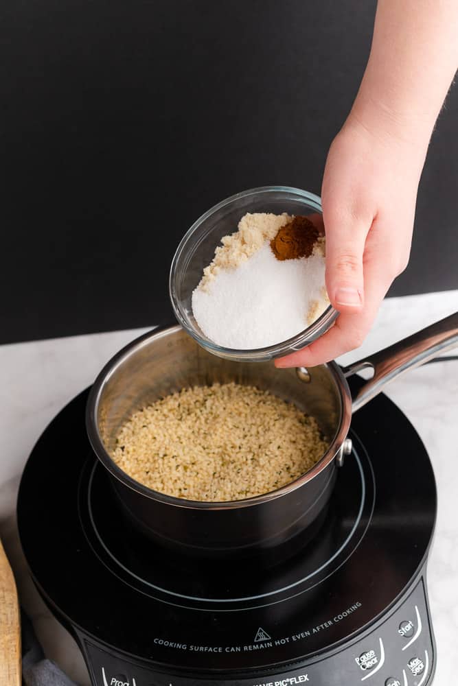 hand pouring cinnamon, sweetener and almond flour to hemp oats