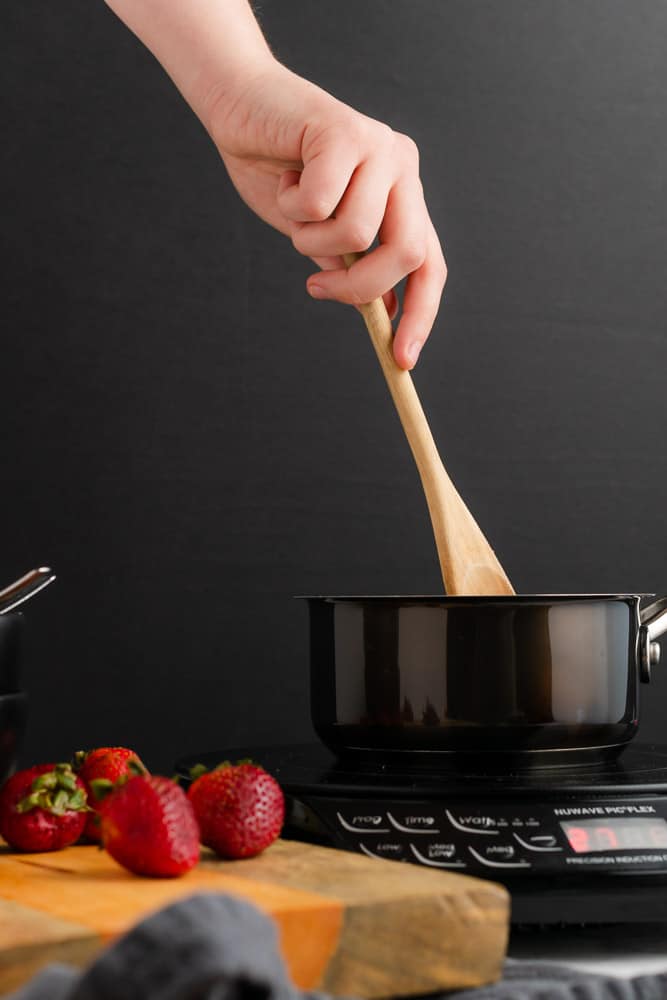 hand stirring wooden spoon in a black saucepan