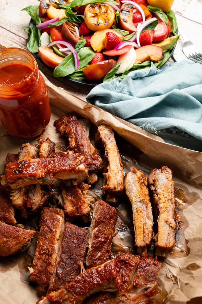 tray of ribs with bbq sauce and peach salad and light blue napkin
