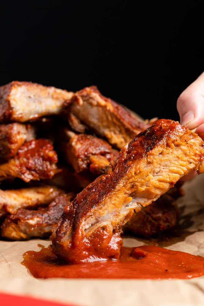hand holding baby back ribs dipping in bbq sauce