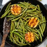 roasted green beans in a cast iron skillet with charred lemons
