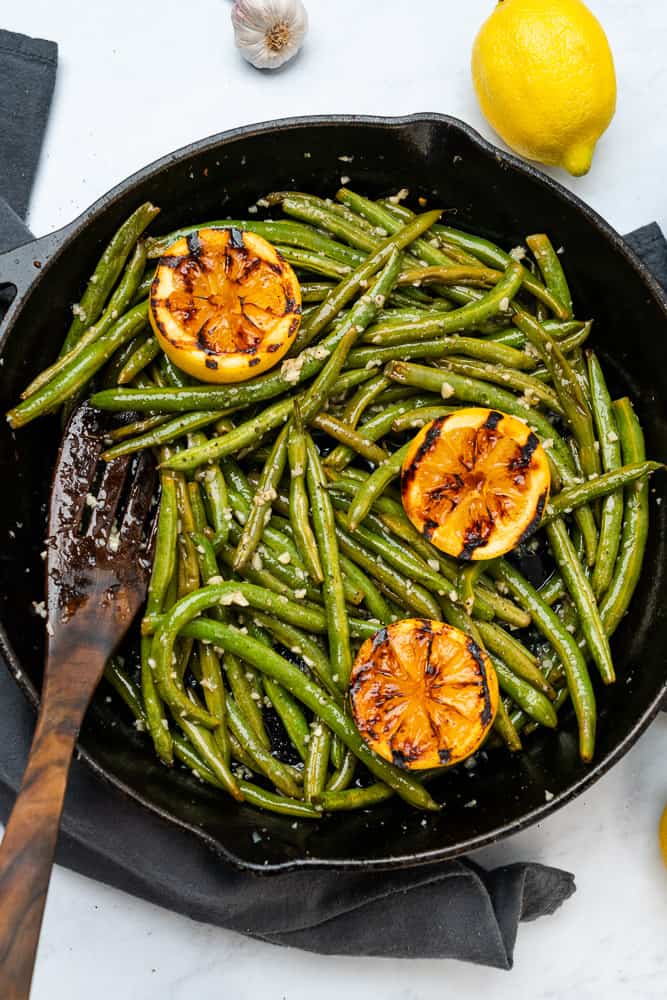 roasted green beans in a cast iron skillet with charred lemons