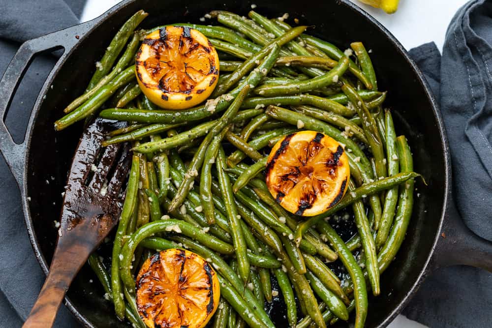 green beans in a skillet with charred lemons