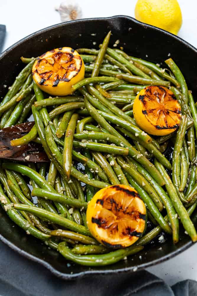 green beans with charred lemons in a skillet with a wooden spoon