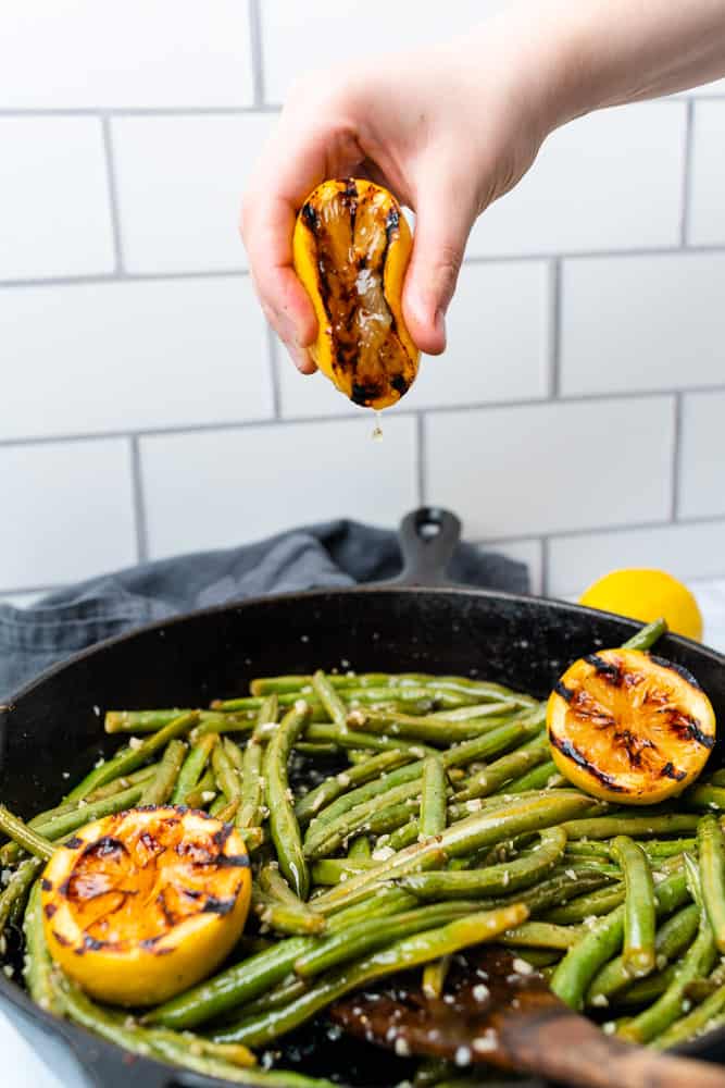 squeezing charred lemon onto a skillet of green beans 