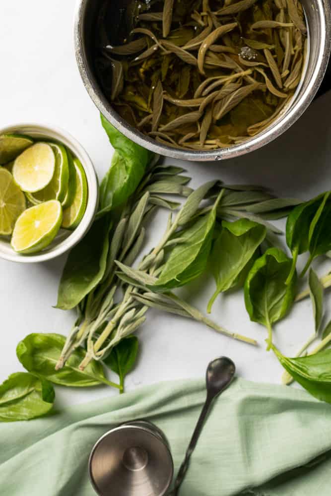 flat lay of basil, sage, limes made into a sugar free keto cocktail syrup