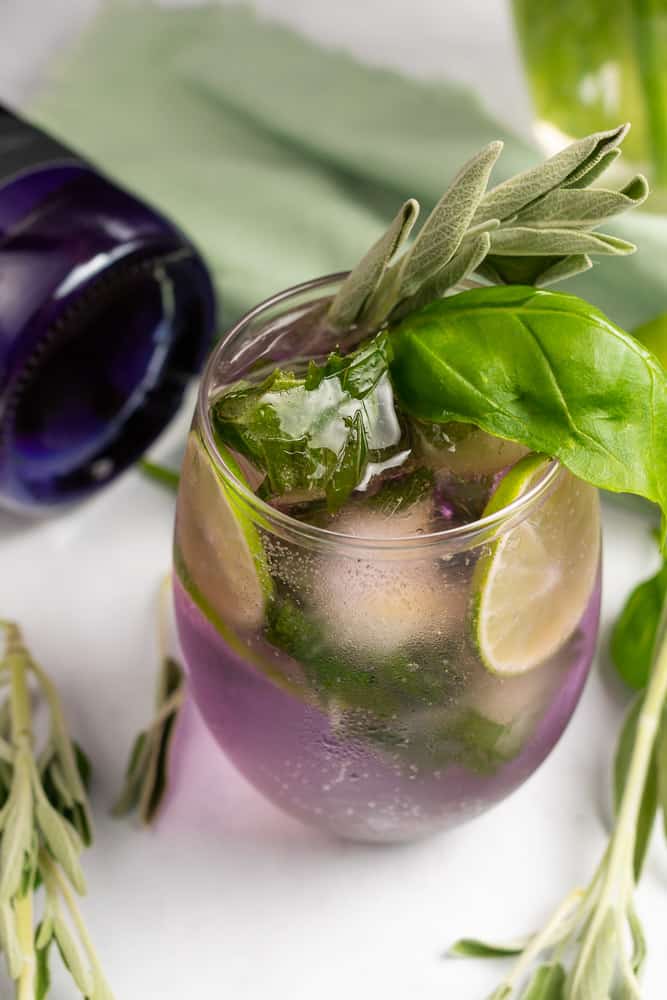 purple gin and tonic with limes, basil and sage
