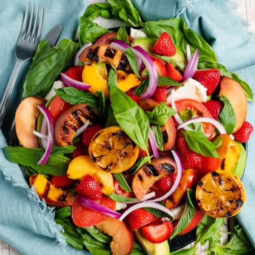 salad with charred lemons, grilled peaches, avocado, mozzarella, strawberries, red onions, tomatoes, basil and mint with a light blue napkin